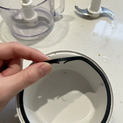A close-up shot of a hand inspecting a rubber gasket seal on a food processor lid for damage or misalignment.