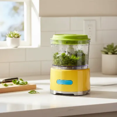 A sleek KitchenAid 3.5-cup mini food processor in a vibrant color on a modern kitchen counter, preparing herbs.